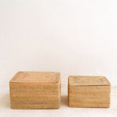 Two woven storage boxes on a light wooden floor with a white wall background