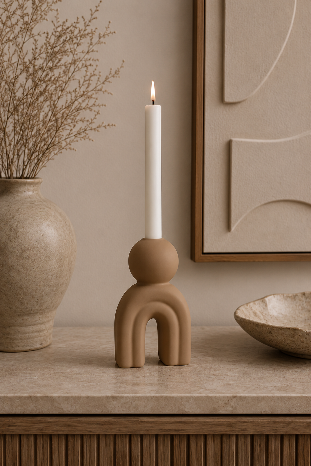 Ceramic candle holder with a lit candle on a neutral-toned surface, with a vase and decorative elements in the background.